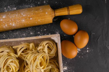 Kırsal ahşap arka planda makarna hazırlamakla geçen bir hayat. Tahta bir kutuda çiğ tagliatelle hamuru ve yumurtası için merdane. Üst Görünüm.