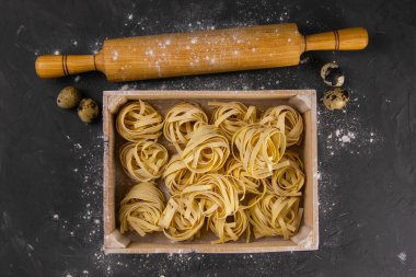 Kırsal ahşap arka planda makarna hazırlamakla geçen bir hayat. Hamur ve bıldırcın yumurtası yerine oklavalı tahta bir kutuda çiğ tagliatelle. Üst Görünüm.