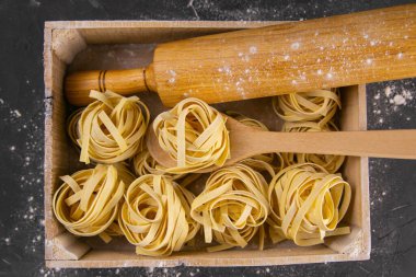 Kırsal ahşap arka planda makarna hazırlamakla geçen bir hayat. Tahta bir kutuda çiğ tagliatelle hamuru için merdane ve tahta kaşıkla. Üst görünüm yakın plan