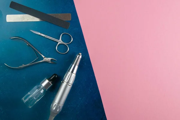 A set of cosmetic tools for manicure and pedicure. Manicure scissors, cuticles, saws, miller stand on a blue and pink background. Top views with clear space.