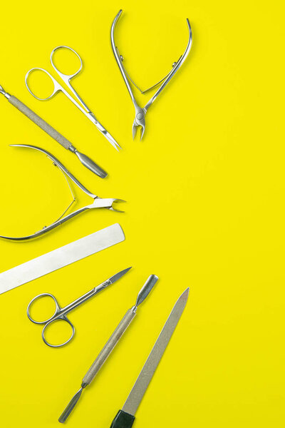 A set of cosmetic tools for manicure and pedicure. Manicure scissors, cutters, nail clippers stand on a yellow background. Top views with clear space.