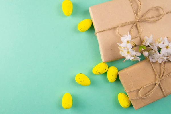 Two easter gifts, yellow eggs and white spring flowers on a mint background close-up. Easter background.