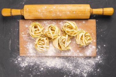 İtalyan ev yapımı çiğ makarna spagettisi ve ahşap tahtanın üzerinde un ve siyah doku arka planında hamur için sallanan tagliatelle çeşitleri. Düz yatıyordu.