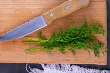 Taze kesilmiş yeşil dereotu ve tahta üzerinde metal bıçak beyaz havlu ve siyah grunge mutfak masası arka planı. Çorba ya da salata eklemek için sebze kesiyorum. Sağlıklı yemek..