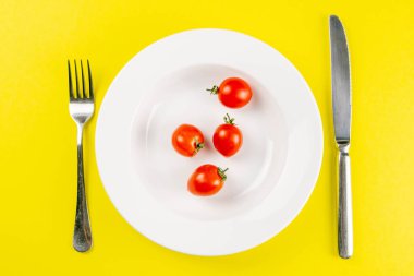 Beyaz tabakta domatesler, arka planda çatal ve bıçak var. Yaratıcı gıda konsepti. Üst Görünüm.