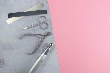 Manikür ve pedikür için kozmetik aletler. Manikür makası, tırnak eti, testere, değirmenci beton pembe arka planda duruyor. Açık alanlı en üstteki görünüm.
