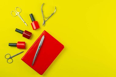 Manikür ve pedikür için kozmetik aletler. Manikür makası, tırnak makasları, testereler, değirmenci ve kırmızı defter arka planda duruyor. Açık alanlı en üstteki görünüm.