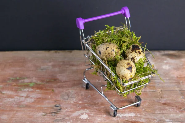 Quail eggs stand in a basket of supermarket filled with moss stand on a wooden table. Top views with clear space.