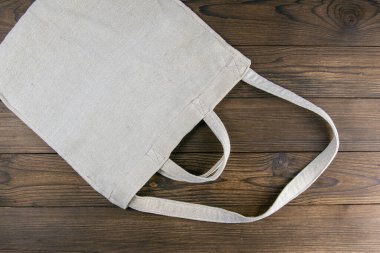 Koyu ahşap masa arkasında çevre dostu beyaz alışveriş torbası. Açık alanlı en üstteki görünüm.