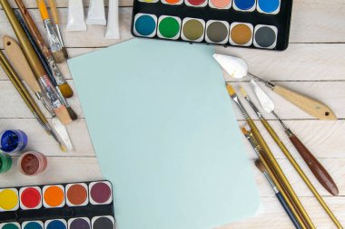 Sanatçı aksesuar koleksiyonu. Tablo, boya tüpü, sanat fırçaları, palet bıçağı ve ahşap masanın üzerinde duran mavi kağıt. Sanatçı atölyesi arka planı.