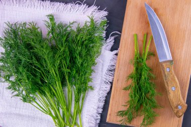 Taze kesilmiş yeşil dereotu ve tahta üzerinde metal bıçak beyaz havlu ve siyah grunge mutfak masası arka planı. Çorba ya da salata eklemek için sebze kesiyorum. Sağlıklı yemek..