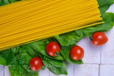 Domatesli çiğ spagetti beyaz ahşap bir masada ıspanak yapraklarının üzerinde duruyor. Üst görünüm, kapat