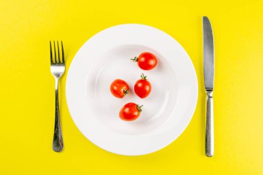 Beyaz tabakta domatesler, arka planda çatal ve bıçak var. Yaratıcı gıda konsepti. Üst Görünüm.