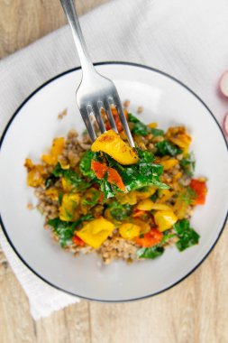 Domatesli, havuçlu, kabaklı, sarı biberli ve açık sade ahşap mutfak masasında taze fesleğenli ev yapımı vejetaryen karabuğday. Üst görünüm, yakın plan