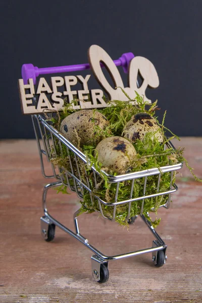 Quail eggs stand in a basket of supermarket filled with moss next is a sign of the Happy Easter stand on a wooden table. Top views.