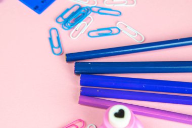 Çok renkli mavi kalemler cetvel, kalem, kalem, makas ve kırtasiye tezgahı pembe arka planda..