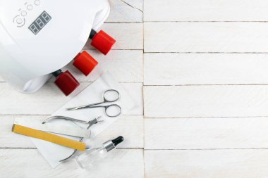 Mavi arka planda manikür ve pedikür için bir takım kozmetik aletler. Manikür lambası, vernik jeli, manikür makası, tırnak derisi ve beyaz havlu standı beyaz ahşap bir masa üzerinde..