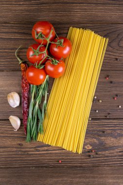 Sebze makarna malzemeleri: spagetti, biber, domates, fesleğen, biberiye, zeytin yağı, sarımsak, deniz tuzu ve koyu ahşap zemin üzerindeki baharatlar. Üst görünüm, yakın plan.