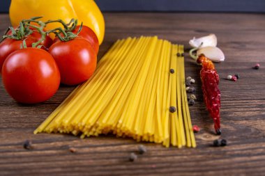 Sebze makarna malzemeleri: spagetti, biber, domates, fesleğen, biberiye, zeytin yağı, sarımsak, deniz tuzu ve koyu ahşap zemin üzerindeki baharatlar. Ön manzara, yakın plan..