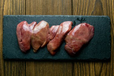 Tahta tahtada çiğ tavuk ciğeri, eski ahşap arka planda. Yemek malzemesi. Üst Görünüm.