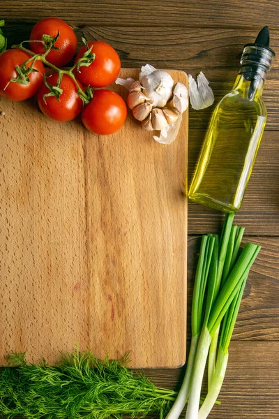 Wooden board with clear space. Around tomato and dill, olive oil, spice, peper, avocado, green onion, spinac and garlic. Top views.