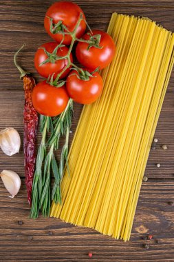 Sebze makarna malzemeleri: spagetti, biber, domates, fesleğen, biberiye, zeytin yağı, sarımsak, deniz tuzu ve koyu ahşap zemin üzerindeki baharatlar. Üst görünüm, yakın plan.