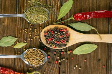 Ahşap bir kaşıkta çok renkli biber, acı kırmızı biber ve ahşap bir masada yan yana serpiştirilmiş. Üst Görünüm.