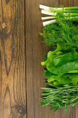 Karışık sebzeler, taze, bahçe bitkileri. Ispanak, biberiye, dereotu ve yeşil soğanlar ahşap bir masada duruyor. Açık alanlı en üstteki görünüm.