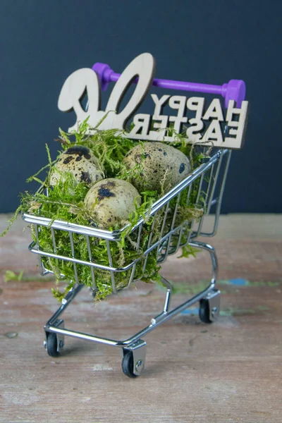 Quail eggs stand in a basket of supermarket filled with moss next is a sign of the Happy Easter stand on a wooden table. Top views.