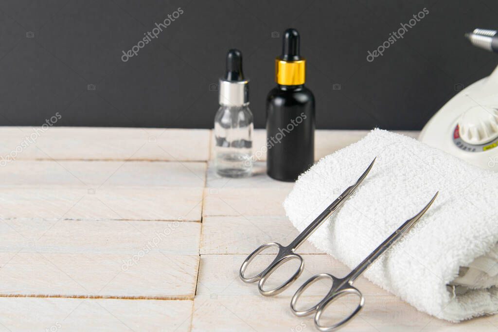 A set of cosmetic tools for manicure and pedicure on a blue background. Fraser, manicure scissors propped up to white towel, in the background are cuticoil oil and hand oil stand on a white wooden background.