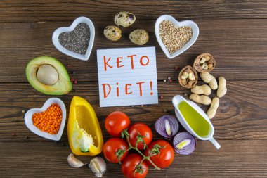 Keto diyeti. Sebzeler ve fındıklar bir çember şeklinde dizilmiş, KETO diyetinin yazılı olduğu bir etiketin içinde. Üst görünüm boşluğu.