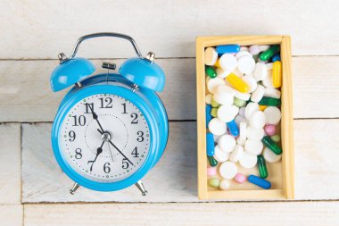 Tablet alma zamanı. Tahta bir kutuda tabletler, beyaz ahşap bir masada mavi bir saat..