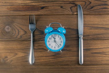 Koyu ahşap masa manzaralı çatal ve bıçaklı klasik bir saat. Klasik renk tonu. Üst Görünüm.