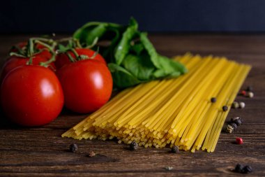 Sebze makarna malzemeleri: spagetti, biber, domates, fesleğen, biberiye, zeytin yağı, sarımsak, deniz tuzu ve koyu ahşap zemin üzerindeki baharatlar. Ön manzara, yakın plan..