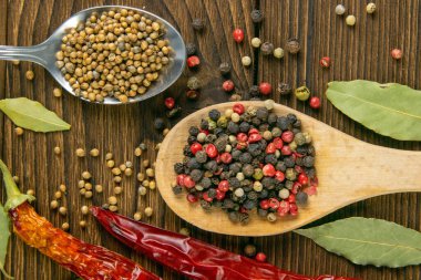 Ahşap bir kaşıkta çok renkli biber, acı kırmızı biber ve ahşap bir masada yan yana serpiştirilmiş. Üst Görünüm.