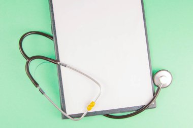 Açık yeşil arkaplan, üst görünüm ve metin için boşluk üzerine tablet ve stetoskop.