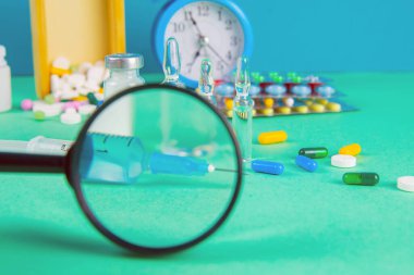 İlaç araştırmaları ve klinik deney konsepti. Aşı enjeksiyonu için ilaç şişesi ve yeni eczane ilacı haplar ve büyüteç altında şırınga..