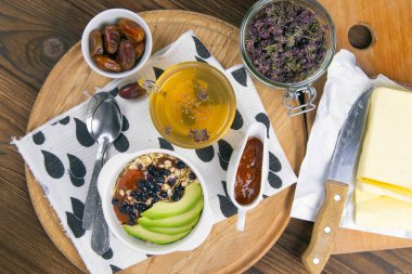 Yanında yoğurt, hurma ve kayısı reçeli bulunan yulaf ezmeli, yabanmersinli ve avokadolu sağlıklı bir kahvaltı. Üst Görünüm.