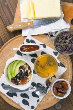 Yanında yoğurt, hurma ve kayısı reçeli bulunan yulaf ezmeli, yabanmersinli ve avokadolu sağlıklı bir kahvaltı. Üst Görünüm.