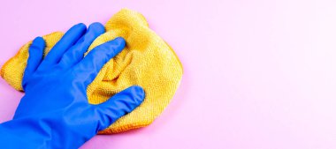 Mavi lastik eldivenli bir kadın. Pembe duvarda sarı bir paçavra tutuyor. Arka planda ise kopya alanı var..