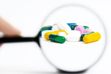 Büyüteç kullanarak hapları yakınlaştırıyorum. Beyaz arka planda izole edilmiş özel haplar.