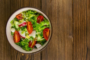 Sağlıklı mutfak kavramı. Taze otlar, turp, salatalık ve domates salatası. Kırsal ahşap arka planda yağlı. Boşluğu kopyala, arkaplan resmi.
