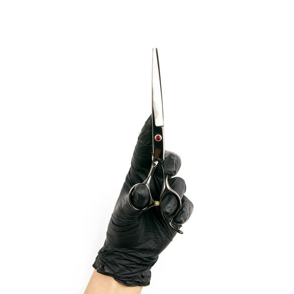 Gloved hand holding a black scisors on an isolated white background.