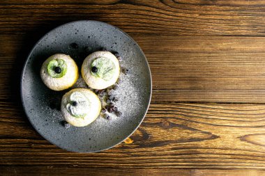 Koyu ahşap masada gri tabakta limonlu ve naneli yaban mersinli kek. Açık alanlı en üstteki görünüm.