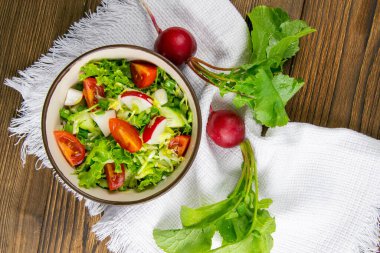 Sağlıklı mutfak kavramı. Taze otlar, turp, salatalık ve domates salatası. Kırsal ahşap arka planda beyaz bir peçetede yağlı. Yakın plan, arkaplan resmi.