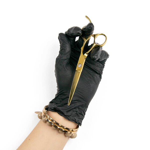 Gloved hand holding a gold scisors on an isolated white background.