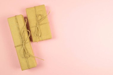 Pembe arka planda el işi kâğıdı ve çuval bezi şeritten yapılmış iki hediye kutusu..