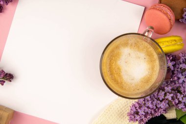 Etrafı leylak renkleri ve renkli badem kurabiyeleriyle çevrili boş bir not kağıdı. Şık, minimalist iş yeri konsepti. Kopyalama alanı olan üst görünüm.