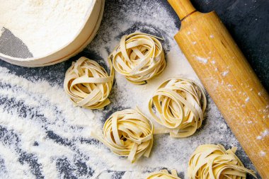 İtalyan ev yapımı çiğ makarna spagettisi ve ahşap tahtanın üzerinde un ve siyah doku arka planında hamur için sallanan tagliatelle çeşitleri. Düz yatıyordu.
