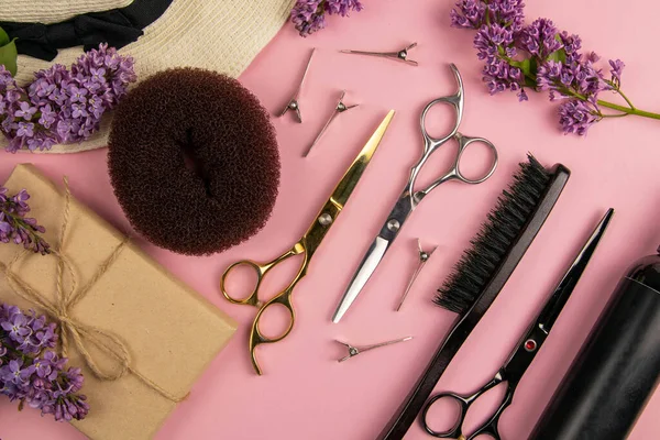 Hairdresser tools - scissors, combs, hairpins and lilac flowers on pink background. Beauty concept. Flat lay, top view.